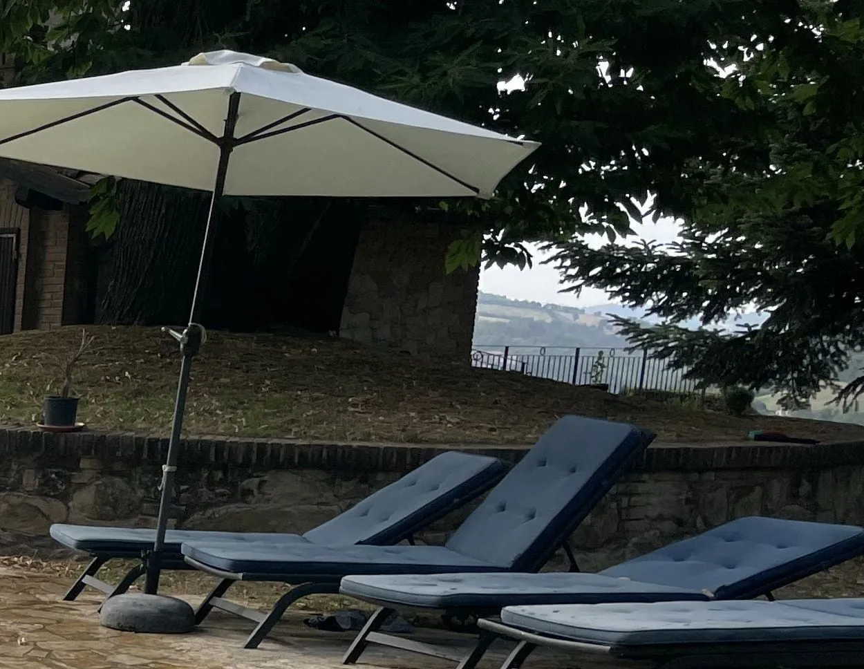 Sun loungers and a parasol in the shade by the pool, with a glimpse of the valley