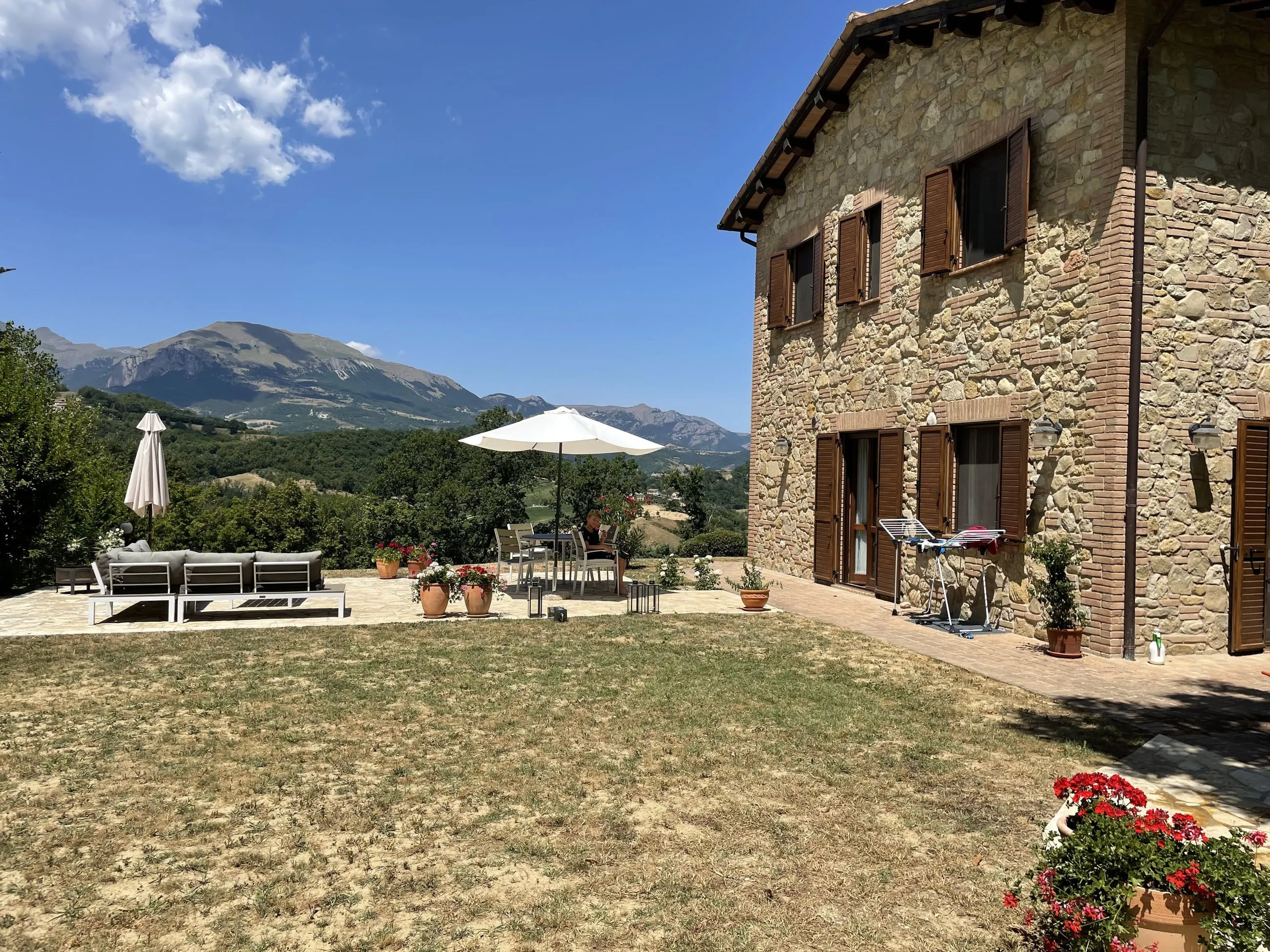 The honey-coloured stone villa with its terrace, parasols and a panorama of Apennine peaks